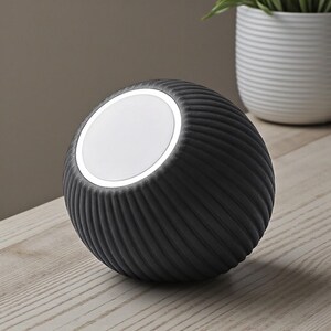 May include: A dark gray, spherical lamp with a textured, ribbed surface. The lamp has a bright, circular light on top. The lamp is sitting on a light-colored wooden surface. A white potted plant is in the background.