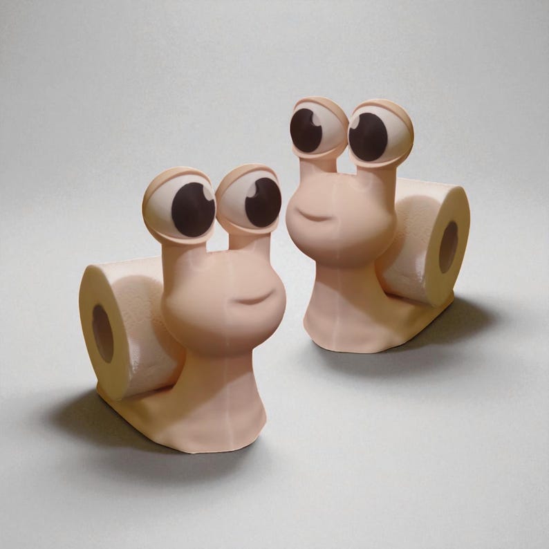 May include: Two whimsical, light pink snail-shaped toilet paper holders. Each holder features large, cartoonish eyes with brown pupils and a smiling face. A roll of white toilet paper is held in place by the snail's body, adding a touch of fun to bathroom decor.