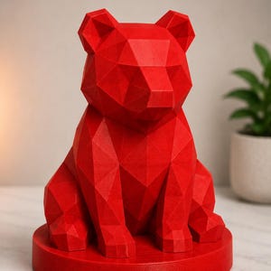 Puede incluir: Una vibrante escultura de oso geom&eacute;trico rojo. El oso est&aacute; sentado sobre una base circular. La escultura est&aacute; hecha de muchas superficies triangulares planas, lo que le da una apariencia facetada. Las orejas del oso est&aacute;n erguidas y sus patas son visibles.