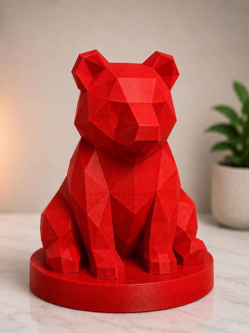 Puede incluir: Una vibrante escultura de oso geom&eacute;trico rojo. El oso est&aacute; sentado sobre una base circular. La escultura est&aacute; hecha de muchas superficies triangulares planas, lo que le da una apariencia facetada. Las orejas del oso est&aacute;n erguidas y sus patas son visibles.