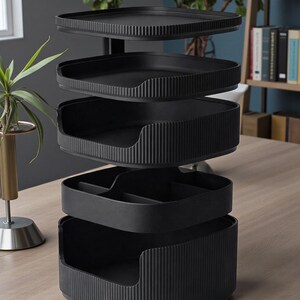 May include: A black, multi-tiered desk organizer with a modern design. The organizer has several trays and compartments for storing office supplies. The trays have a ribbed texture. The organizer is made of a matte black material.