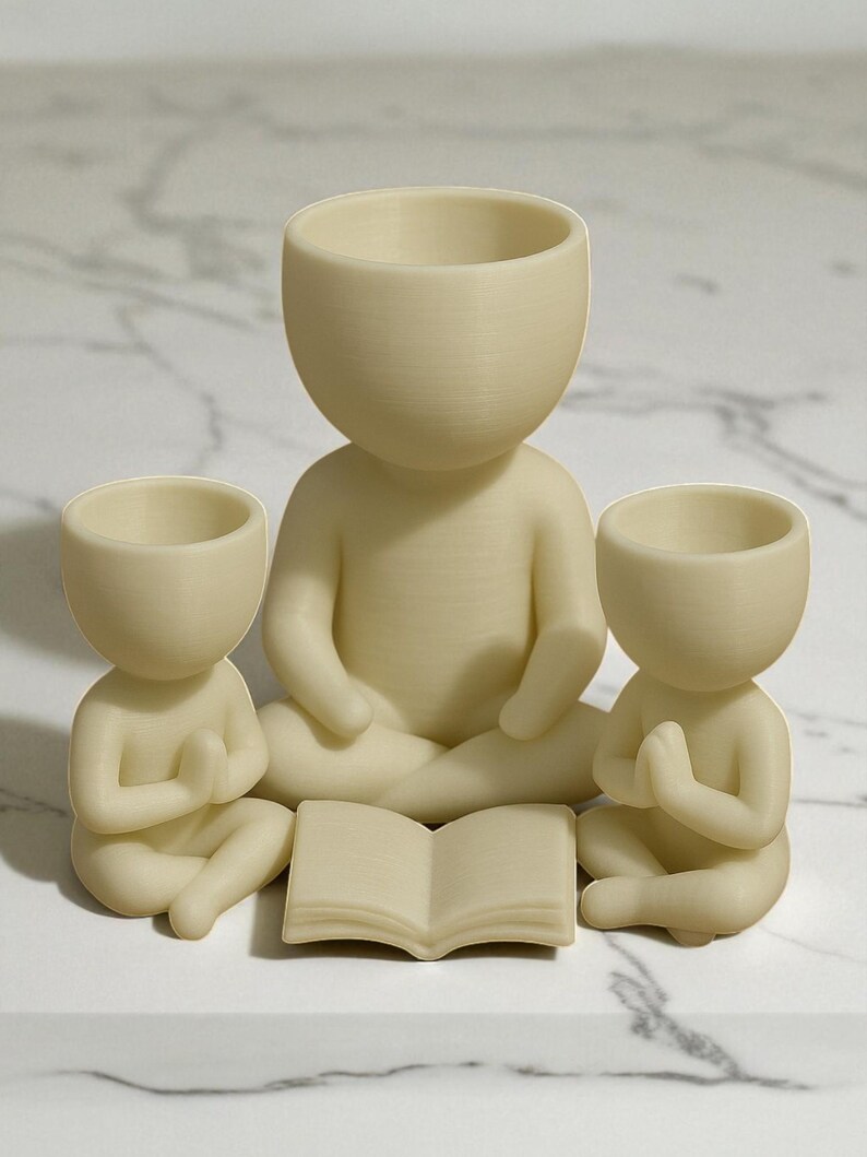 May include: Three cream-colored, seated human-shaped planters. The largest figure is in the center, with two smaller figures on either side. An open book is in front of the central figure. The planters have open tops for plants.