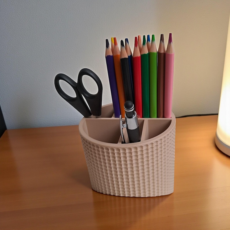 May include: A beige desk organizer with a woven texture, holding colored pencils, a black pen, and scissors. The pencils are various colors, including red, green, and purple. The organizer sits on a wooden surface.