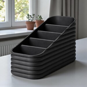 May include: A black desk organizer with a tiered design. The organizer has five compartments and a ribbed exterior. The product is made of a matte black material and sits on a white surface.