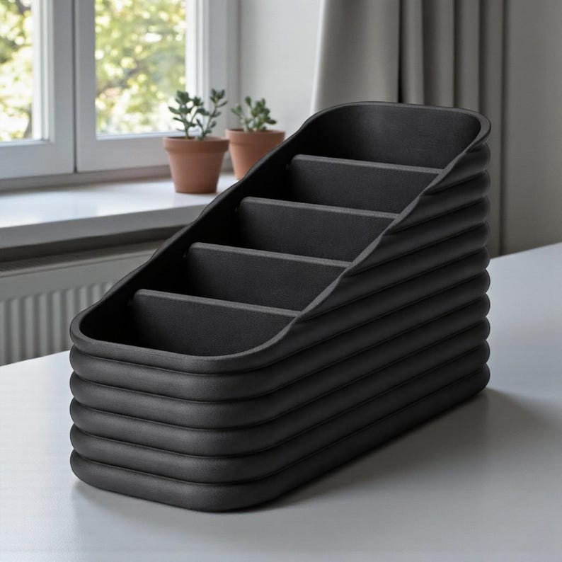 May include: A black desk organizer with a tiered design. The organizer has five compartments and a ribbed exterior. The product is made of a matte black material and sits on a white surface.