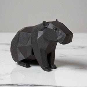 May include: A black geometric capybara sculpture. The stylized figure has a faceted design, giving it a modern, angular appearance. The sculpture is made of a solid, dark material and sits on a white marble surface.