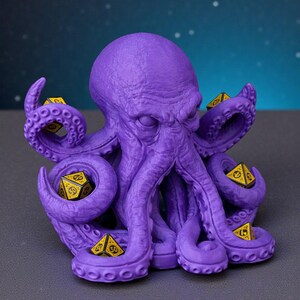May include: A purple octopus-shaped dice holder with multiple tentacles, each holding a yellow and black die. The octopus has a textured surface and is set against a dark background. The dice are standard size.