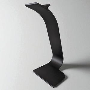 May include: A modern, black metal desk lamp with a curved, minimalist design. The lamp features a rectangular base and a slender, arched stem that supports a small, flat head. The overall aesthetic is sleek and contemporary.