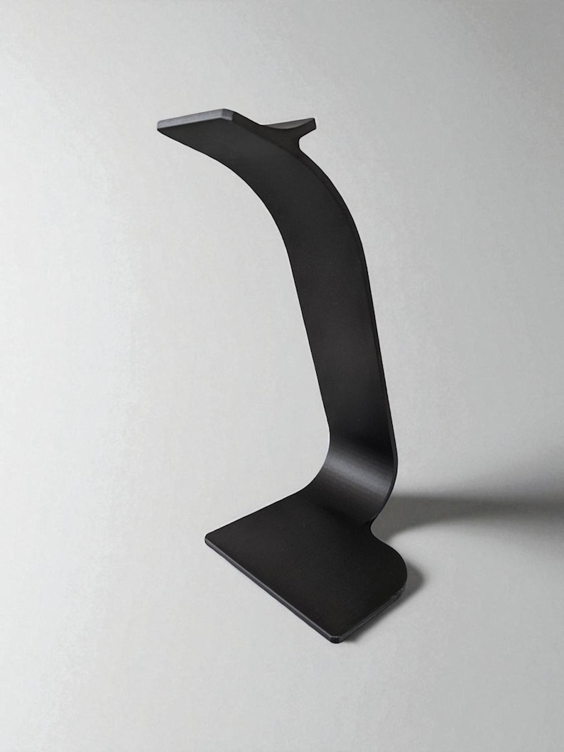 May include: A modern, black metal desk lamp with a curved, minimalist design. The lamp features a rectangular base and a slender, arched stem that supports a small, flat head. The overall aesthetic is sleek and contemporary.