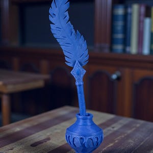 May include: A blue inkwell with a decorative feather quill. The inkwell has a detailed, ornate design and sits on a wooden table. The feather quill is upright, and the background includes a bookshelf and warm lighting.
