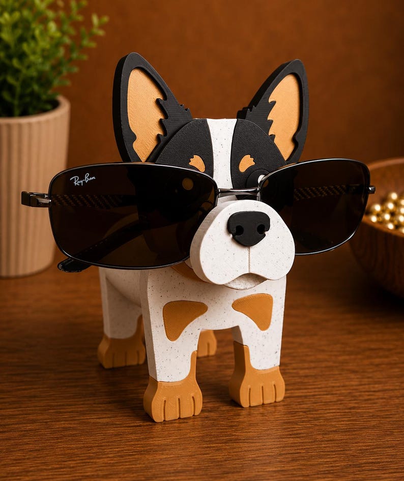May include: A wooden dog-shaped eyeglass holder with a black nose and sunglasses. The dog is white with brown and black accents. The sunglasses are dark-tinted with the Ray-Ban logo on the left lens. The holder is on a wooden surface.
