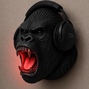 May include: A black gorilla head sculpture with an open mouth and red glowing interior. The gorilla wears black headphones. The sculpture is mounted on a neutral-colored wall.