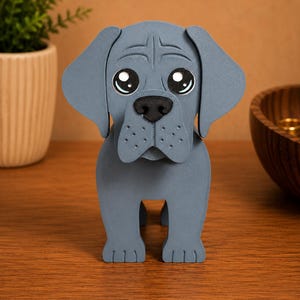 May include: A gray, stylized dog figurine with large, expressive eyes and a black nose. The dog has floppy ears and a textured surface, giving it a handcrafted appearance. The figurine is standing upright on a wooden surface.