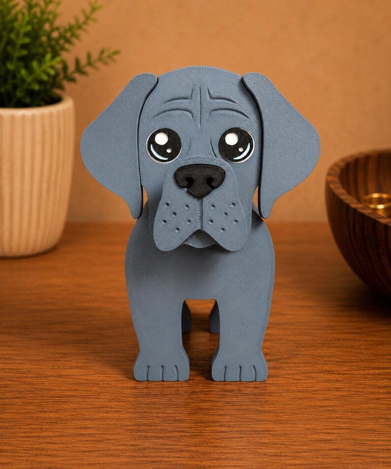 May include: A gray, stylized dog figurine with large, expressive eyes and a black nose. The dog has floppy ears and a textured surface, giving it a handcrafted appearance. The figurine is standing upright on a wooden surface.
