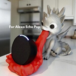 May include: A silver dragon-shaped speaker holder with a red tongue holding a black speaker. The text "For Alexa Echo Pop" is visible. The speaker has a black mesh front and a white light.