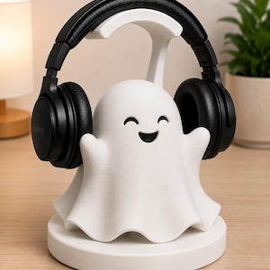 May include: A white ghost-shaped headphone stand with a smiling face, holding a pair of black headphones. The stand is on a round base. The headphones are black with the brand name "SONY" visible on the ear cup.