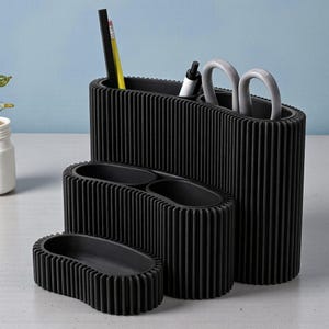 May include: A set of four black desk tidies in different sizes. The ribbed design containers hold pens, pencils, and scissors. The background is a light blue.