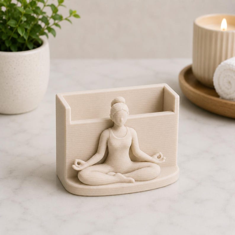 May include: A beige-colored desk organizer featuring a sculpted figure of a person in a seated yoga pose. The organizer has a rectangular shape with a slot for pens or small items. The figure is in a meditative position.
