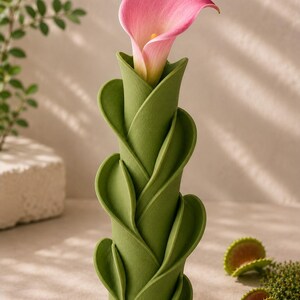 May include: A green, leaf-shaped vase holds a pink calla lily. The vase has a unique, spiraling design. The background includes a small plant and a few Venus flytraps.