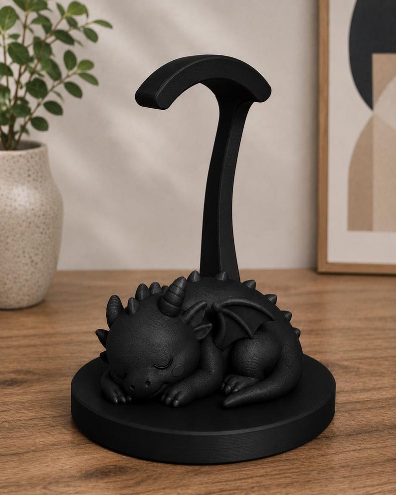May include: A black dragon-shaped headphone stand. The dragon is sleeping on a round base, with a tall, curved support for headphones. The stand is made of a matte black material and is designed to hold headphones.