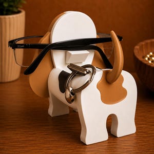 May include: A wooden eyeglasses and key holder shaped like a beagle dog. The holder is painted white with brown and black spots, and a tan tail and ears. Black eyeglasses rest on the dog's head, and keys hang from the nose.