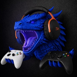 May include: A blue dragon head wall mount featuring a textured scale pattern and glowing eyes. The dragon wears black and orange over-ear headphones and uses its blue claws to hold a white game controller on the left and a black game controller on the right.