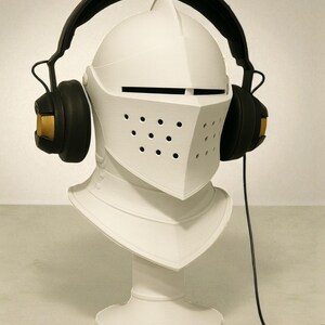 May include: A white knight's helmet bust with black headphones. The headphones have gold accents on the earcups. The helmet features a visor with small holes and a neck guard. A black cable extends from the headphones.