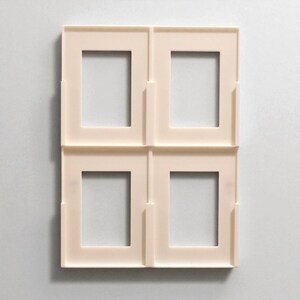 Pu&ograve; includere: Quattro cornici quadrate color crema disposte in una griglia 2x2. Ogni cornice ha un'apertura rettangolare al centro. Le cornici sono realizzate in un materiale liscio e opaco e sono progettate per contenere fotografie o opere d'arte.