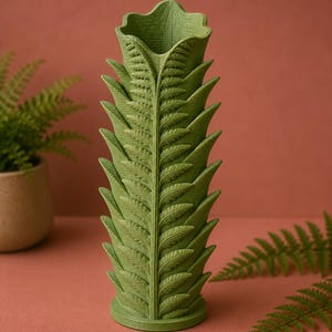 Pu&ograve; includere: Un vaso verde a forma di felce con dettagli intricati delle foglie. Il vaso ha una forma cilindrica con una parte superiore svasata e una base rotonda. Il colore &egrave; un verde tenue e il design imita la struttura di una fronda di felce. Lo sfondo &egrave; un marrone rossastro tenue.