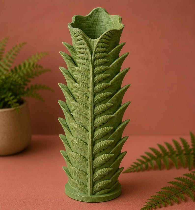 Pu&ograve; includere: Un vaso verde a forma di felce con dettagli intricati delle foglie. Il vaso ha una forma cilindrica con una parte superiore svasata e una base rotonda. Il colore &egrave; un verde tenue e il design imita la struttura di una fronda di felce. Lo sfondo &egrave; un marrone rossastro tenue.