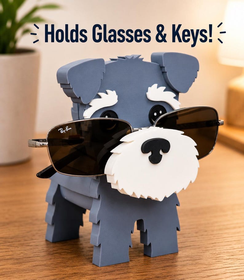 May include: A gray dog-shaped glasses holder with a white beard and black nose, holding sunglasses. The text "Holds Glasses & Keys!" is above the dog. The sunglasses are Ray-Ban brand.