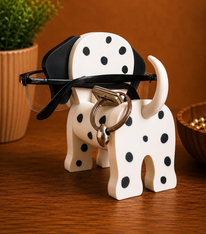 K&ouml;nnte beinhalten: Ein wei&szlig;-schwarz gefleckter Brillen- und Schl&uuml;sselhalter in Form eines Dalmatiners. Der Halter hat einen Schlitz f&uuml;r Brillen und einen Ring f&uuml;r Schl&uuml;ssel. Der Hunde-Halter ist aus Holz gefertigt und hat schwarze Ohren und schwarze Flecken.