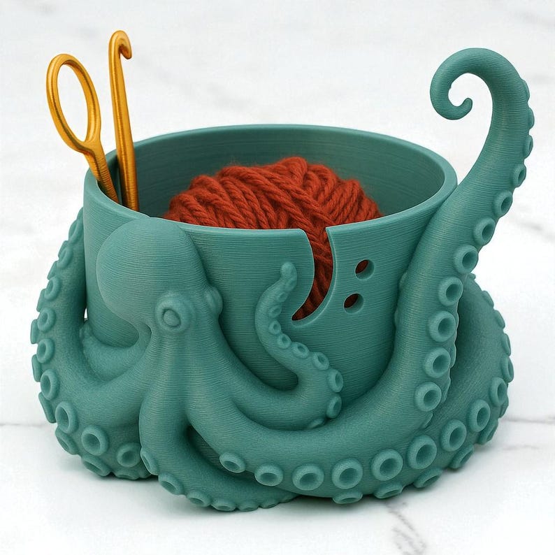 May include: A teal octopus-shaped yarn bowl with a ball of orange yarn inside. Two gold crochet hooks are placed in the bowl. The bowl has a unique design with tentacles and suction cups, perfect for holding yarn and tools.