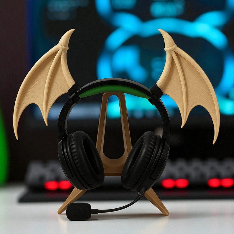 May include: Black gaming headphones with a microphone, resting on a wooden stand shaped like a bat. The stand has two beige wings attached to the top. The headphones have a green band and are on a white surface.