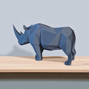 May include: A dark gray geometric rhino sculpture with a prominent horn. The rhino is standing on a light brown wooden shelf against a gray wall. The sculpture has a faceted design, giving it a modern look.
