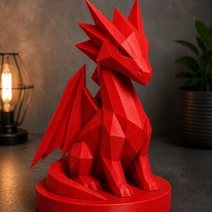 May include: A red geometric dragon sculpture with sharp angles and detailed wings. The dragon is seated on a circular base. The sculpture is a decorative item, suitable for home decor or as a unique gift.