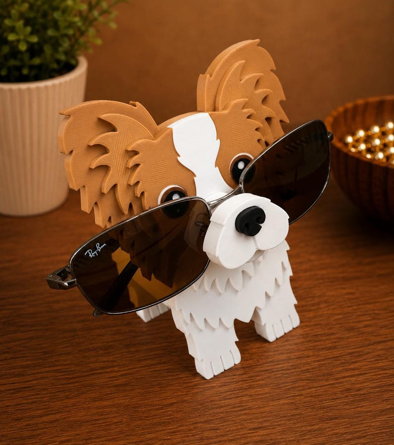 May include: A decorative wooden dog-shaped sunglasses holder. The dog is white with brown and tan accents and is wearing Ray-Ban sunglasses. The holder is on a wooden surface.