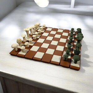 May include: A novelty chess set with mushroom-shaped pieces in cream and green. The board has a brown and cream checkered pattern. The pieces are detailed, adding a whimsical touch to the classic game. The set is displayed on a light-coloured surface.