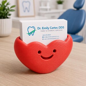 May include: A red heart-shaped business card holder with a smiling face. The holder contains white business cards with the text "Dr. Emily Carter, DDS, Family & Cosmetic Dentistry."