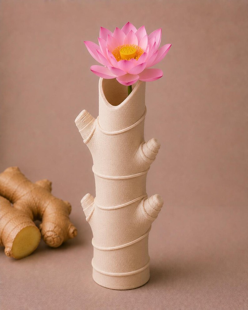 Op de afbeelding: Een beige keramische vaas in de vorm van een gemberwortel, met een roze lotusbloem. De vaas heeft een textuur en decoratieve details. De bloem heeft roze bloemblaadjes en een gele kern.