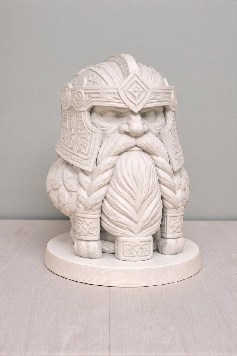 May include: An off-white sculpture of a dwarf with a detailed helmet and braided beard. The sculpture is mounted on a round base. The helmet and beard feature intricate carvings. A decorative item.