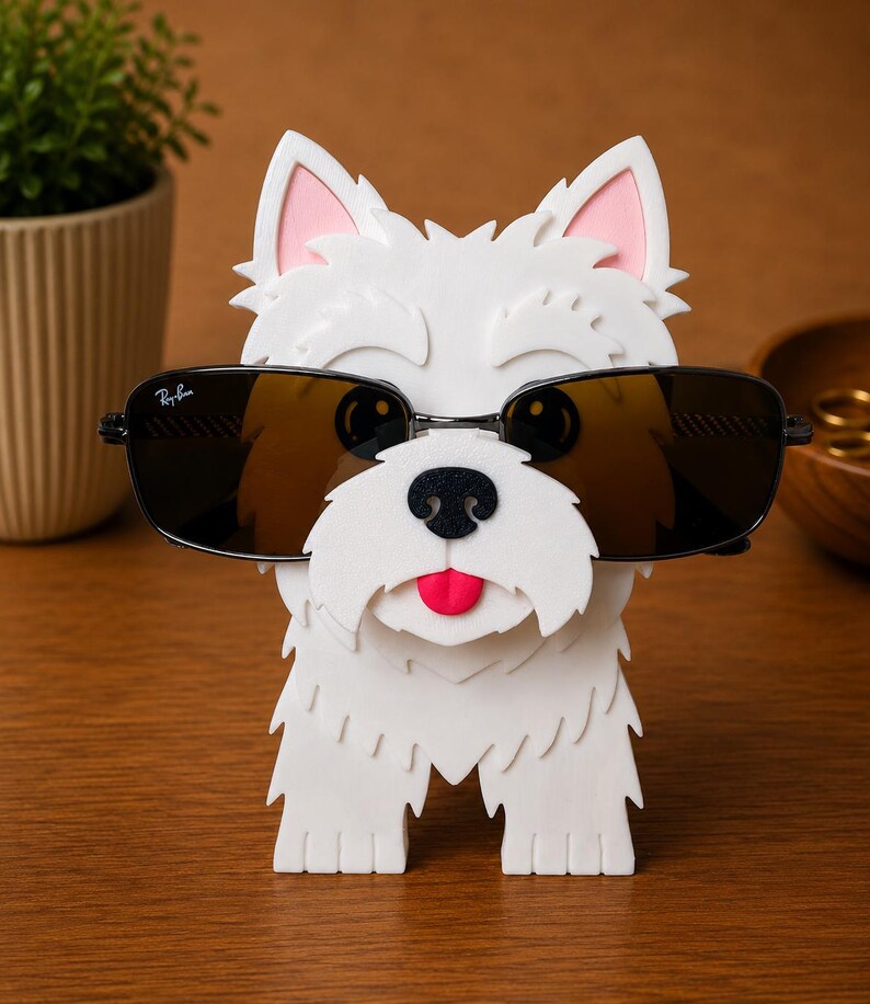 May include: A white dog-shaped eyeglass holder with a black nose, pink ears, and a red tongue. The holder is wearing black sunglasses with a Ray-Ban logo. The holder is made of a textured material and sits on a wooden surface.