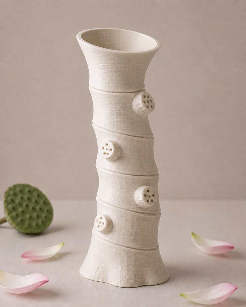 May include: A cream ceramic vase with a textured, bamboo-style design. The vase has four circular, pod-like accents with small holes. Pink and white flower petals and a green seed pod are scattered around the base of the vase.