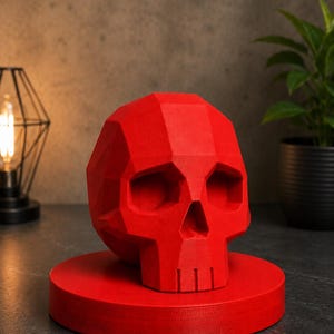 May include: A vibrant red, geometric skull sculpture, resting on a matching circular base. The skull features a faceted design, creating a modern, artistic aesthetic. This decorative piece is ideal for adding a unique touch to home decor.