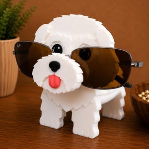 May include: A white dog-shaped sunglasses holder with black eyes, a black nose, and a red tongue. The holder is wearing brown sunglasses. The holder is made of a solid material and is sitting on a wooden surface.