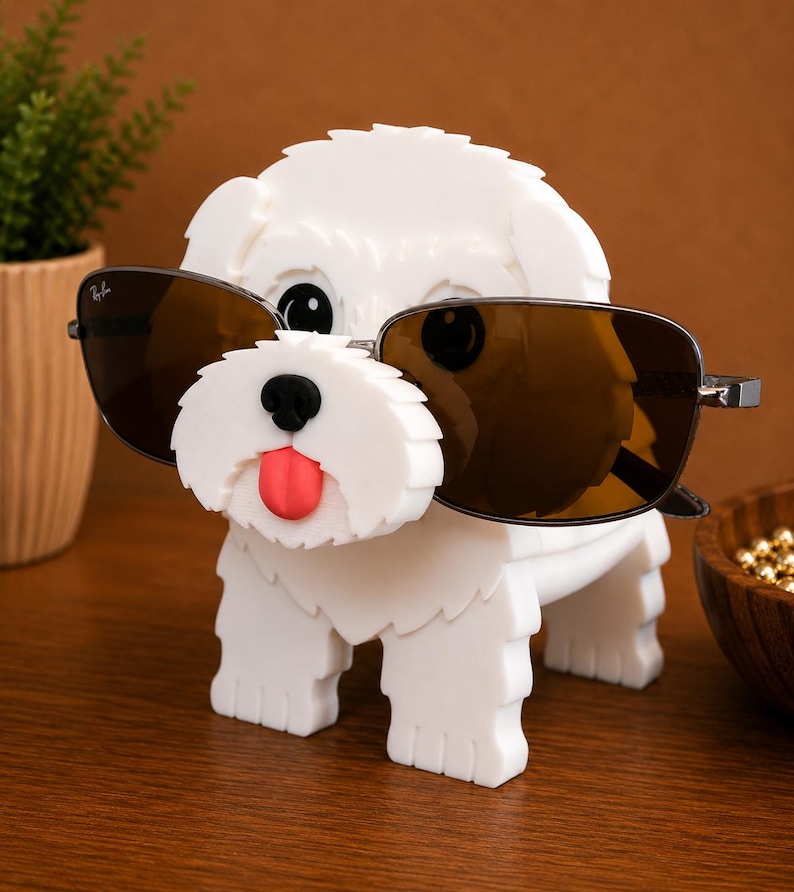 May include: A white dog-shaped sunglasses holder with black eyes, a black nose, and a red tongue. The holder is wearing brown sunglasses. The holder is made of a solid material and is sitting on a wooden surface.