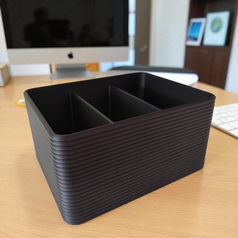 K&ouml;nnte beinhalten: Ein dunkelbrauner Schreibtisch-Organizer mit drei F&auml;chern. Der Organizer hat eine geriffelte Au&szlig;enseite und steht auf einem hellen Holzschreibtisch. Der Hintergrund umfasst einen Computermonitor und eine Tastatur.