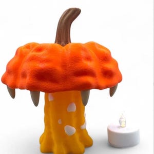May include: A whimsical orange mushroom-shaped lamp with a brown stem and three fang-like protrusions. The lamp has a yellow base with white spots. A small, battery-operated candle sits beside the lamp. Halloween decor.