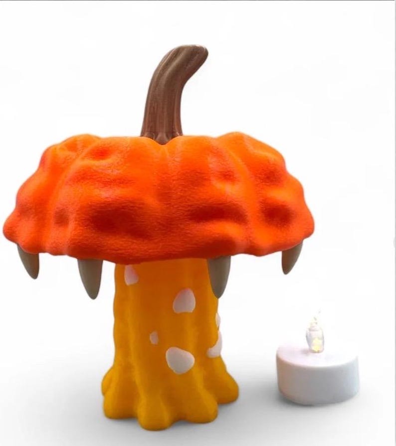 May include: A whimsical orange mushroom-shaped lamp with a brown stem and three fang-like protrusions. The lamp has a yellow base with white spots. A small, battery-operated candle sits beside the lamp. Halloween decor.