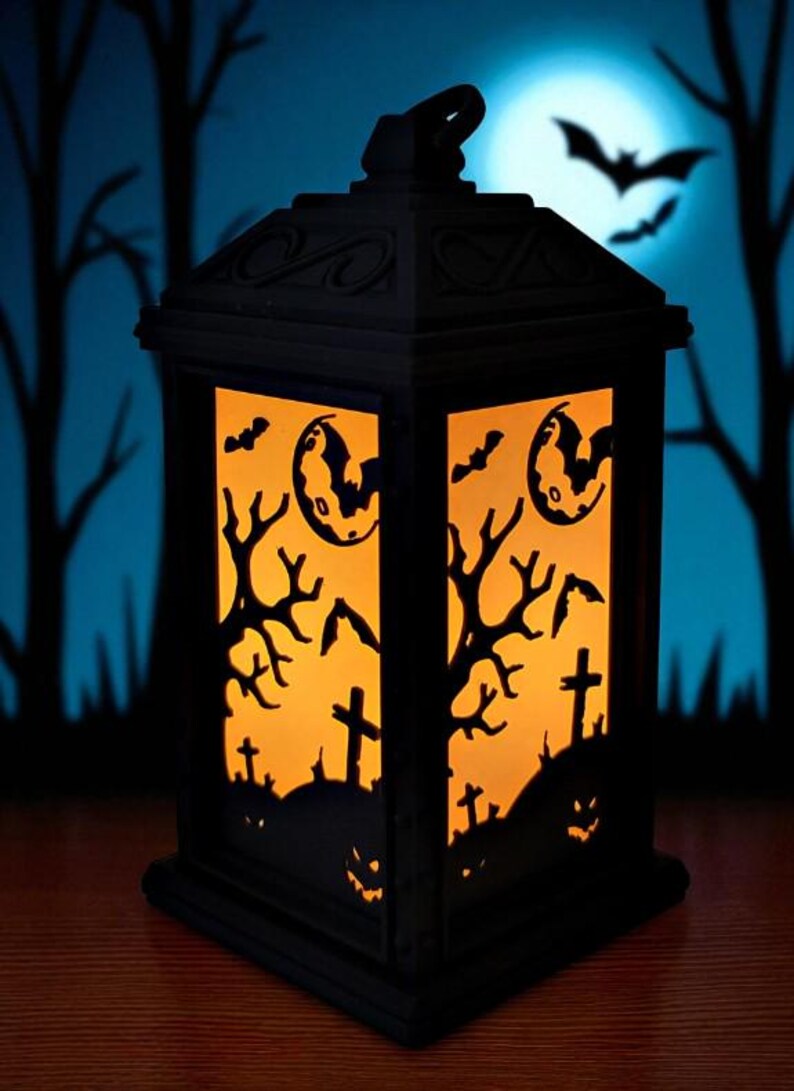 May include: Black Halloween lantern with orange interior light. The lantern features cut-out designs of bats, a full moon, bare trees, crosses, and jack-o'-lantern faces. The background shows a blue sky with a full moon and silhouettes of trees.